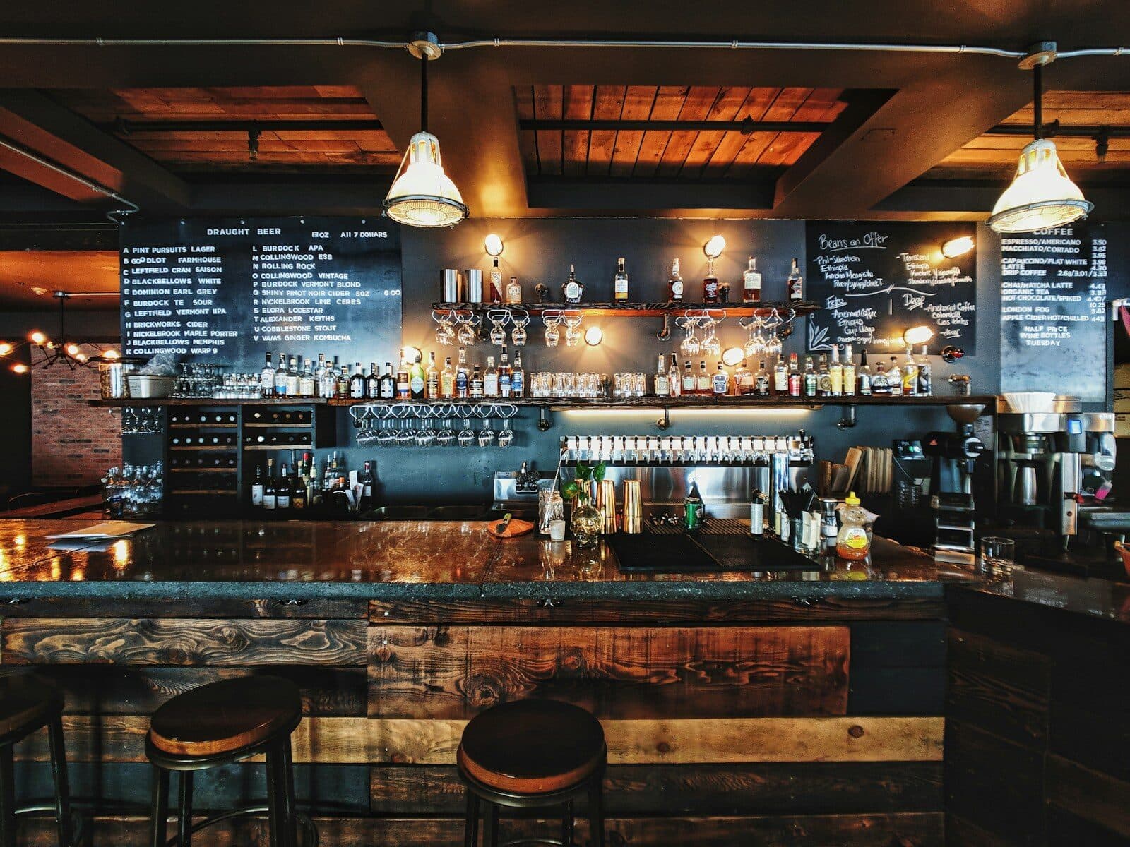 Restaurant bar at night with backlit bottles, pendant lamps and wooden stools