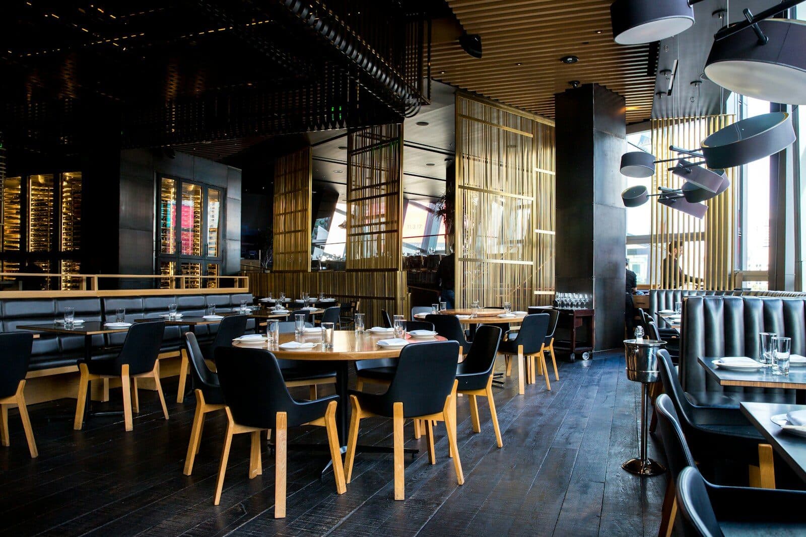 Dark restaurant dining room with black chairs, set tables and warm pendant lights