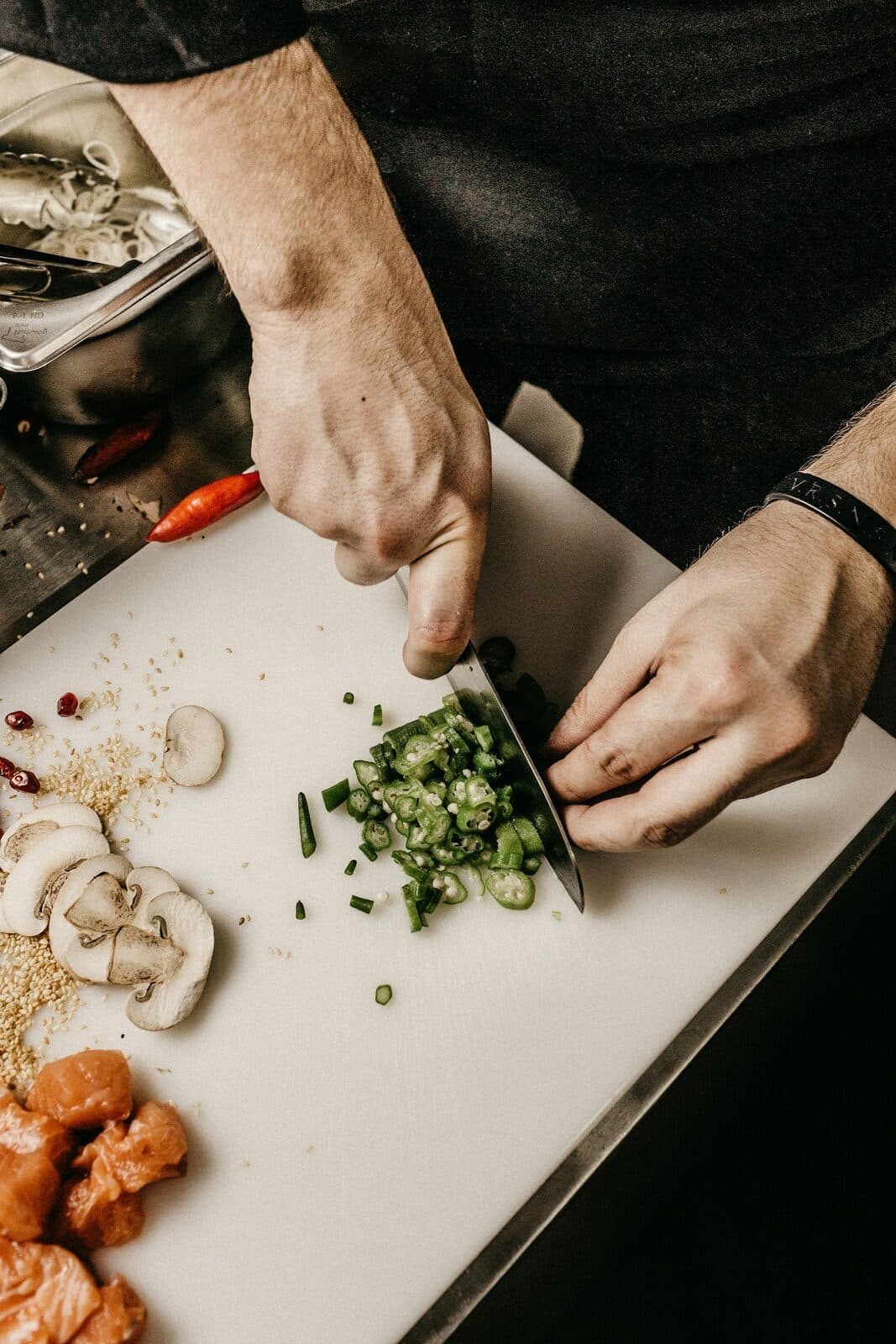 Chef's hands chopping herbs on a cutting board beside a knife and mushrooms