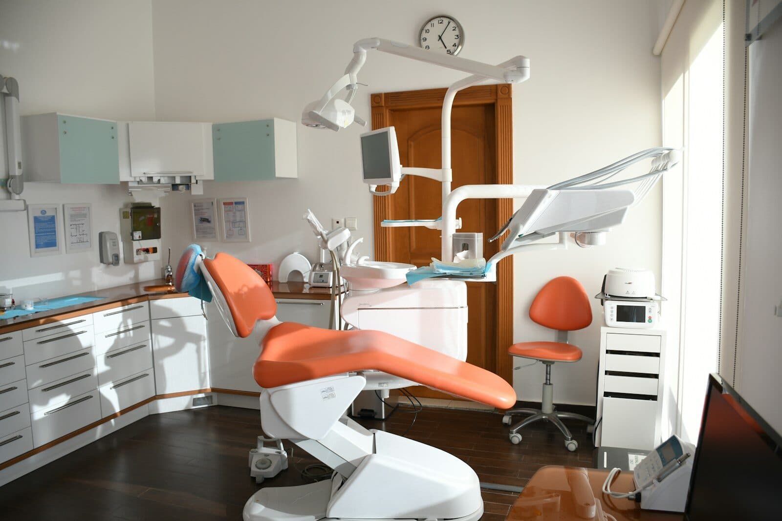Dental treatment room with an orange dental chair, white cabinets and a window
