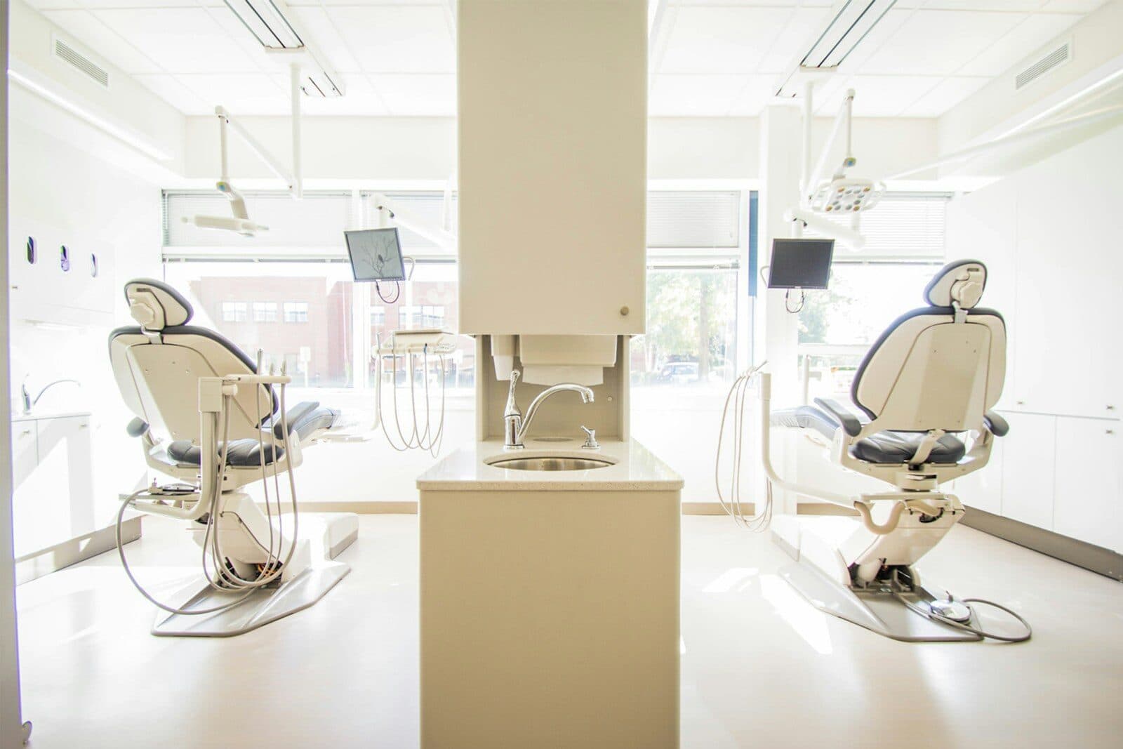 Bright dental treatment room with two dental chairs beside floor-to-ceiling windows