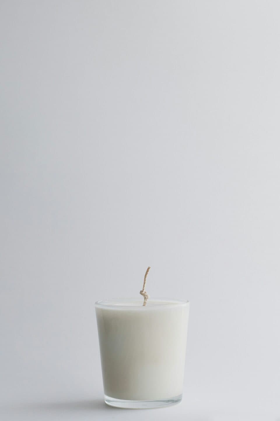 A white candle in a glass jar on a plain background