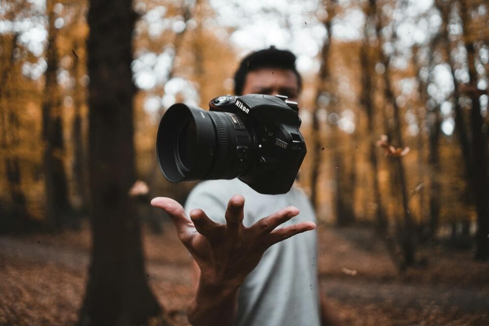 Photographer tossing a camera into the air in autumn woods